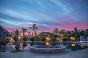 a resort pool with palm trees and a sunset at Cerritos Surf Town - Beach Front Property in El Pescadero