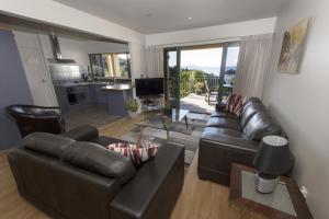 a living room with two leather couches and a kitchen at Allegra House in Paihia