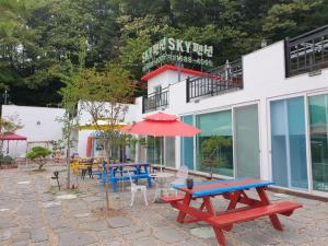 un grupo de mesas de picnic y una sombrilla frente a un edificio en Sky Vivaldi Pension en Hongcheon