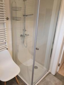 a shower with a glass door with a white chair at Apartament nad Sapiną in Kruklanki