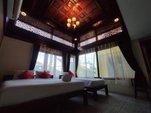 a bedroom with two beds with windows and a ceiling at Ban Mae Boonthong in Lampang