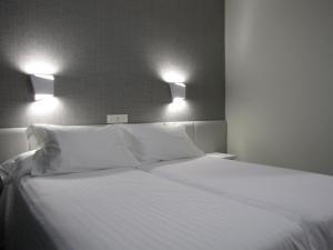 a white bed with two pillows and two lights above it at Hotel Ton in Sanxenxo