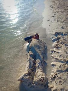 a man buried in the sand in the water at شاليهات بورتو مطروح فيو بحر Porto Matrouh Sea View Families Only in Marsa Matruh