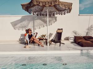 a woman sitting in a chair under an umbrella next to a swimming pool at Playa del Mar - Adults Only in Monopoli