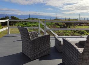eine Terrasse mit Korbstühlen, einem Tisch und einem Zaun in der Unterkunft Varandas do Basalto in Queimada