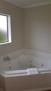 Tudor Lodge Motel في هاويرا: حمام أبيض مع حوض استحمام ونافذة