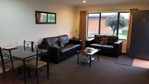 a living room with two leather couches and a table at Tudor Lodge Motel in Hawera