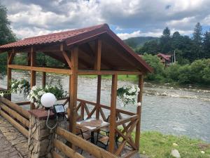 un cenador de madera con una mesa junto a un río en Villa Bilogirya en Yaremche