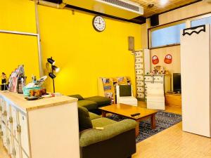 un salon avec un mur jaune et une horloge dans l'établissement Hostel Furoya, à Osaka