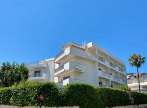 un bâtiment blanc avec un palmier en face dans l'établissement Résidence Carlton - Entièrement rénové, à Beaulieu-sur-Mer