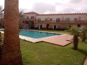 - une piscine en face d'un bâtiment avec un palmier dans l'établissement Duplex, à El Jadida