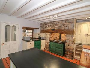 a kitchen with green cabinets and a stone wall at Bawbee Cottage in Denbigh