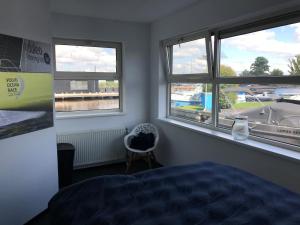 a bedroom with three windows and a bed and a chair at The Boathouse with boat in Aalsmeer