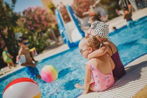 una mujer y una niña sentadas junto a una piscina en Caesar Resort & SPA en Trikomo