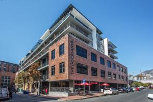 a large brick building with red umbrellas on a street at Docklands Deluxe One bedroom Apartments in Cape Town