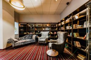 a library with two chairs and a couch and bookshelves at Hotel Palcát in Tábor