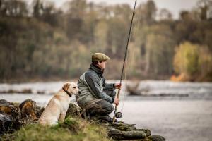 a man and a dog sitting next to a river with a rod at The Gleneagles Hotel in Auchterarder