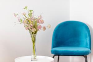 eine Vase mit Blumen auf einem Tisch neben einem blauen Stuhl in der Unterkunft Globo - self check-in hostel in Šibenik