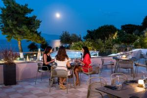 three women sitting at tables on a patio at night at Porto Galini Seaside Resort & Spa in Nikiana