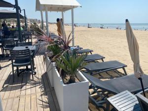 - une plage avec des chaises, des tables et un parasol dans l'établissement Acadie Saint Victor - Hôtel restaurant - Face mer - Chatelaillon plage, à Châtelaillon-Plage