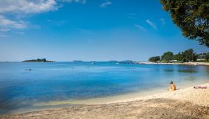 un hombre sentado en una playa cerca del agua en Maistra Camping Polari Mobile homes, en Rovinj