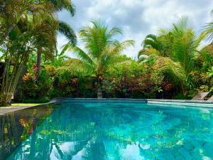 a swimming pool with palm trees in the background at Pondok Naya - CHSE Certified in Ubud