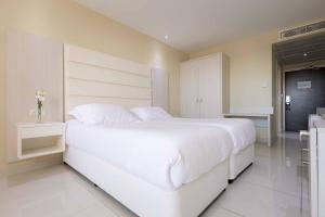 a white bedroom with a large white bed and a kitchen at Tasia Maris Beach Hotel - Adults Only in Ayia Napa