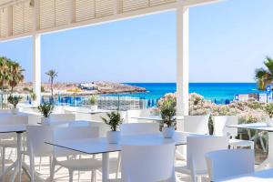 a restaurant with white tables and chairs and the ocean at Tasia Maris Beach Hotel - Adults Only in Ayia Napa