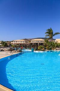 a large blue swimming pool with buildings in the background at Natura Park Village Hotel & Spa in Psalidi