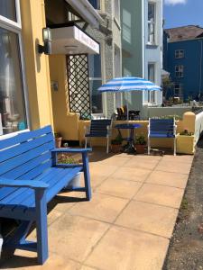 eine blaue Bank und zwei Tische mit Sonnenschirmen auf einer Terrasse in der Unterkunft Awel Mor in Criccieth