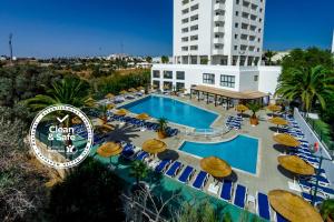 ein Pool mit Sonnenschirmen und Stühlen sowie ein Gebäude in der Unterkunft Janelas do Mar Apartamentos Turisticos in Albufeira