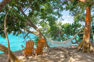 two chairs and a hammock under a tree on the beach at Hotel San Pedro de Majagua in Isla Grande