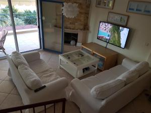 a living room with white couches and a flat screen tv at PANORAMA HOUSE in Metókhion Konstamonítou