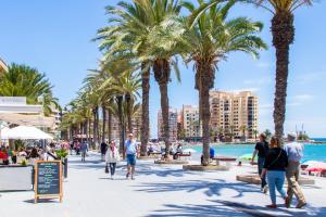 Menschen gehen auf einem Bürgersteig neben einem Strand mit Palmen in der Unterkunft Apartamento Playa del Cura in Torrevieja