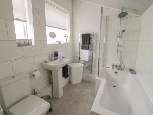 a white bathroom with a sink and a tub and a toilet at Thimble Cottage in Cheltenham