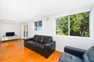 a living room with a black leather couch and two windows at Bonny Beach House in Bonny Hills