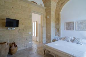 a bedroom with a bed and a tv on a stone wall at Li Perrini Boutique B&B in Acquarica
