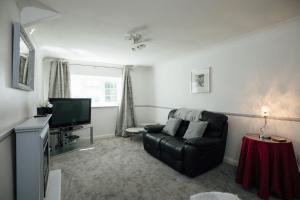 a living room with a black leather couch and a television at Mews Flat in Tenby