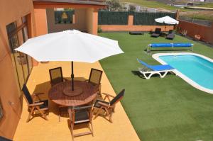 a table with an umbrella next to a swimming pool at ECO Villa White Suite with climatized pool in Caleta De Fuste