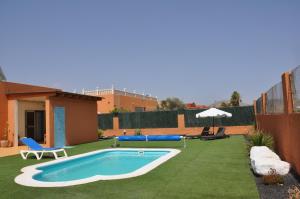 a backyard with a swimming pool and green grass at ECO Villa White Suite with climatized pool in Caleta De Fuste