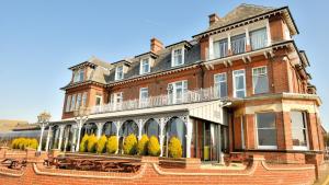 um grande edifício de tijolos vermelhos com árvores em frente em Wherry Hotel em Lowestoft