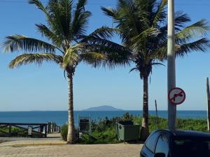 two palm trees on a beach with the ocean in the background at Vila de Sol in Bombinhas
