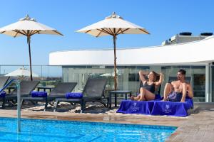 a man and woman sitting on towels next to a swimming pool at Jupiter Marina Hotel - Couples & Spa in Portimão