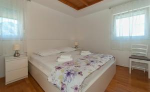 a white bedroom with a bed with a floral bedspread at Apartment Luna in Omiš