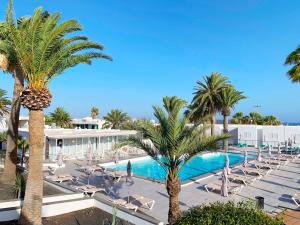 ein Resort mit einem Pool, Palmen und Stühlen in der Unterkunft Apartamentos Arena Dorada in Puerto del Carmen