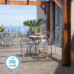 a table and chairs on a patio with the ocean in the background at Casa das Proteas in São Jorge