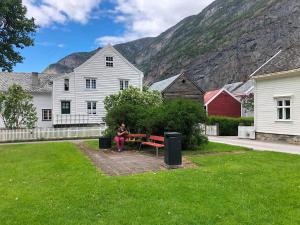 a woman sitting on a bench in a yard at Den Gule Krambua - Gamle Lærdalsøyri - main street old town in Lærdalsøyri