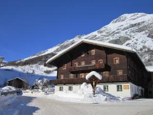 a large wooden building covered in snow in front of a mountain at Hansenhof in Prägraten