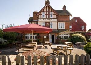 un pub con mesas y bancos y una sombrilla roja en Raven Hotel by Greene King Inns, en Hook