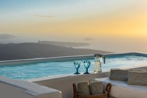 a pool with two wine glasses and a table at Aqua Luxury Suites Santorini in Imerovigli